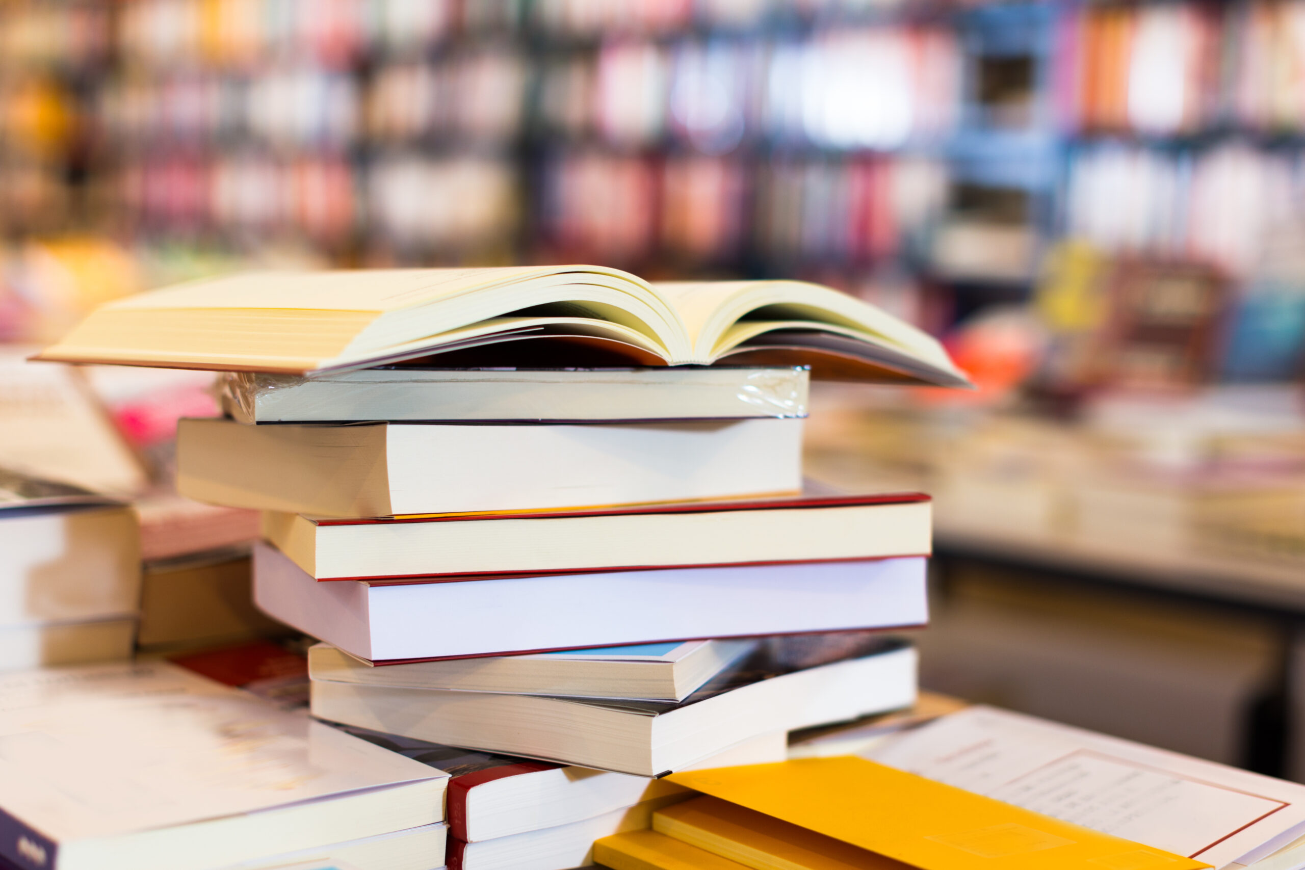 Photograph of a stack of books lying on a table in a library, with the top book on the pile open.