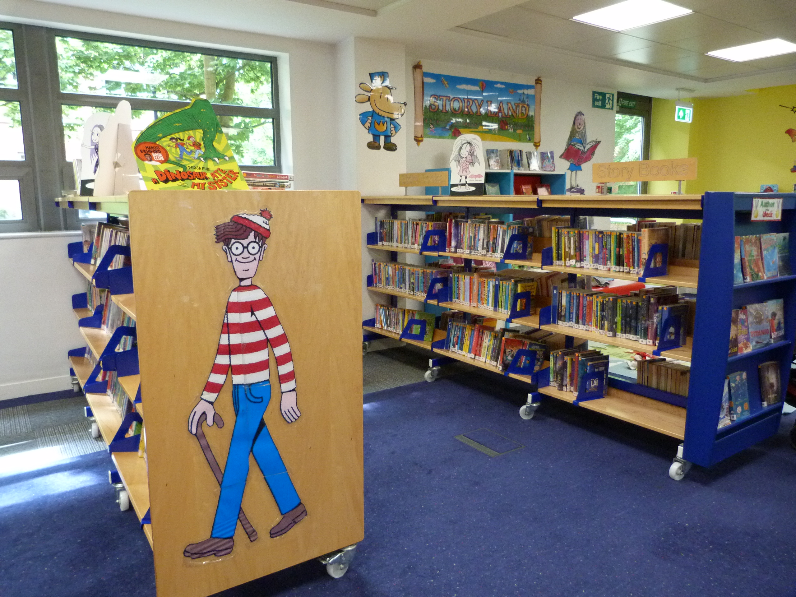 Photograph of shelves of childrens books in Huyton Library with a where's Wally display image.