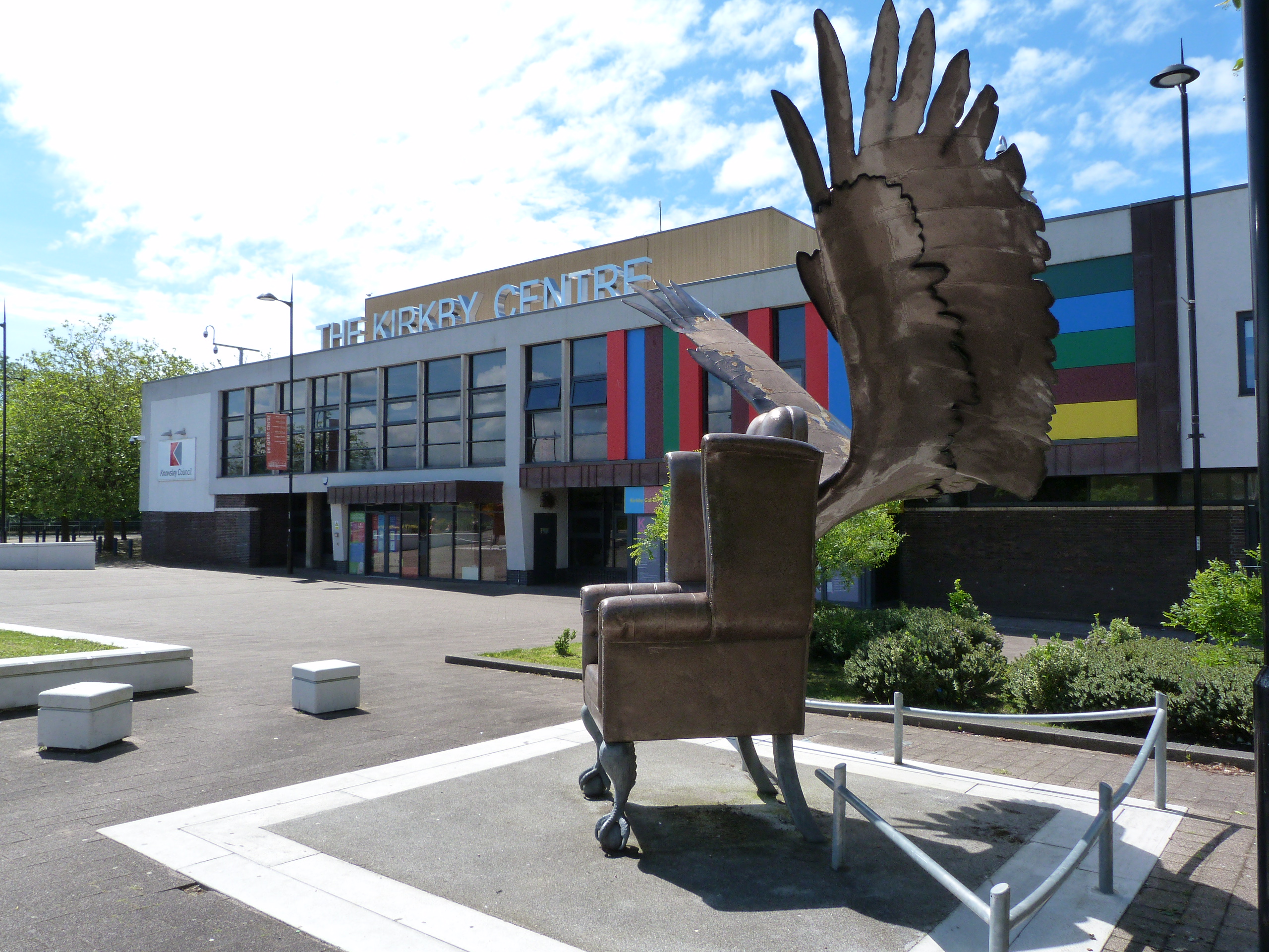 Photograph of the exterior of Kirkby Library showing an armchair with wings art sculpture in the foreground.