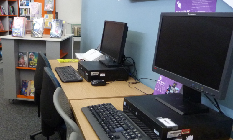 Photograph of 2 public desktop computers at Prescot Library, with book display unit in the background