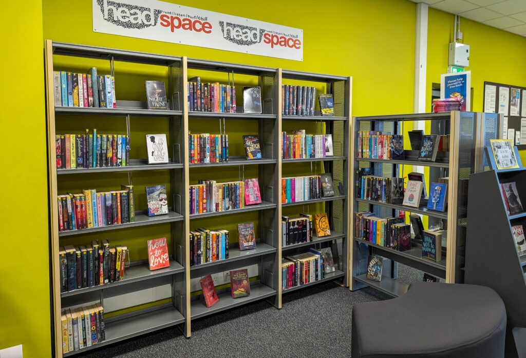 Photograph of interior of Halewood Library's Head Space teenage area, showing book shelves in front of light green wall.